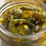A close-up of sliced Cowboy Candy jalapeños in brine inside a glass jar.