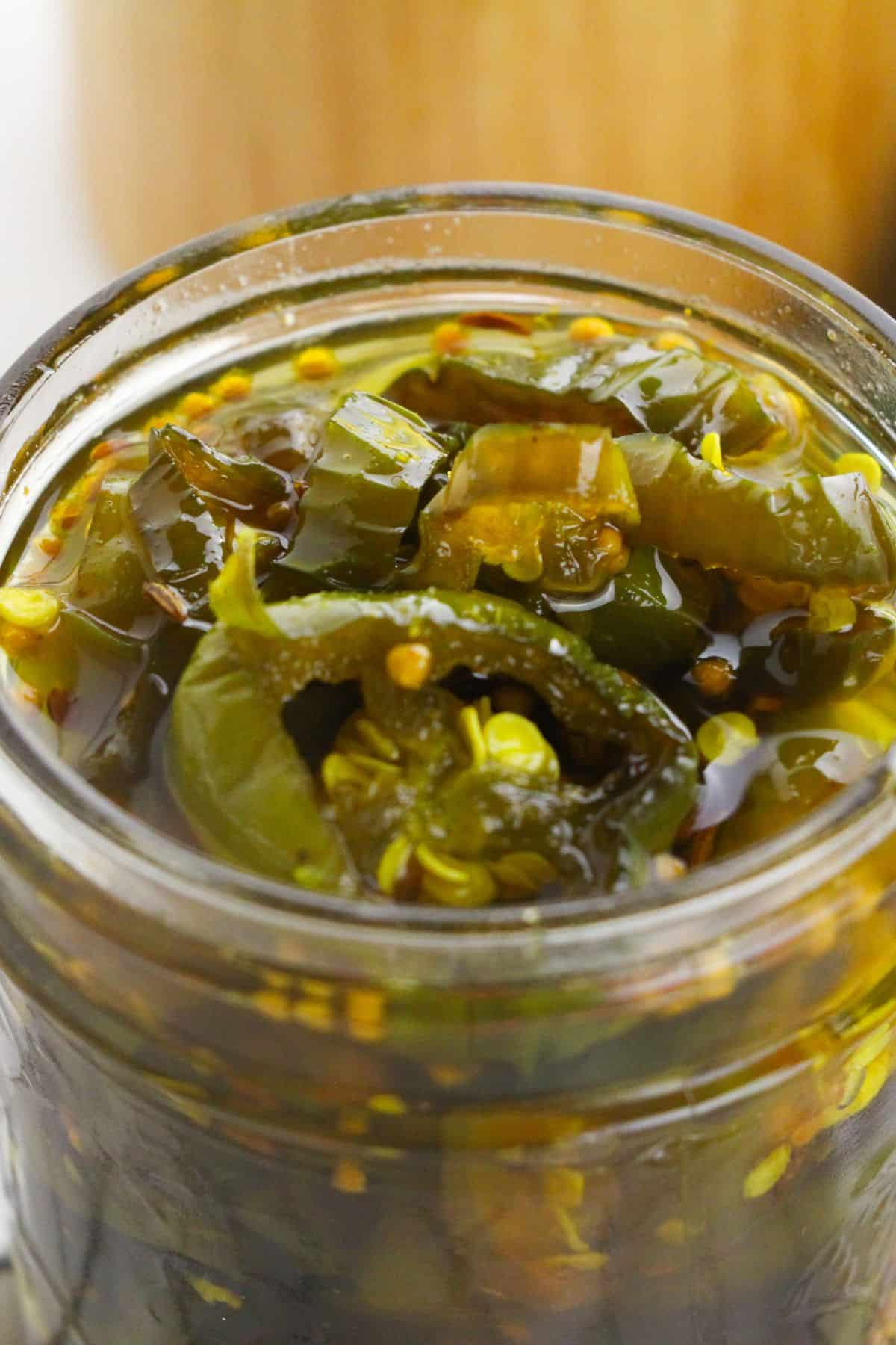 A close-up of sliced Cowboy Candy jalapeños in brine inside a glass jar.