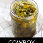 A glass jar filled with sliced Cowboy Candy—jalapeños in syrup—rests on a white cloth with a black grid pattern. The text "COWBOY CANDY" is displayed at the bottom.