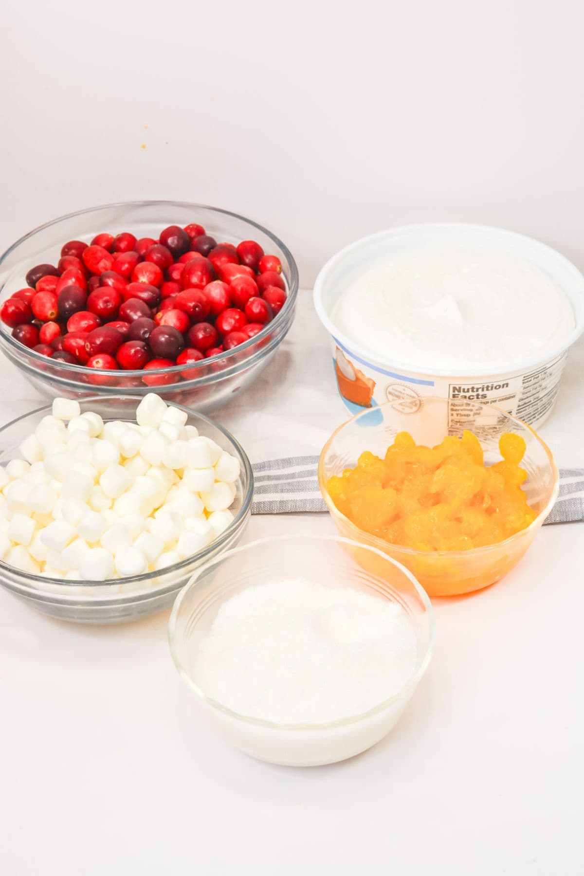 Five bowls hold the classic ingredients—fresh berries, whipped topping, mini marshmallows, crushed pineapple, and shredded coconut—perfect for crafting this festive dessert or holiday recipe.