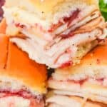 Three stacked Cranberry Turkey Sliders feature melted cheese and cranberry sauce nestled on soft dinner rolls.
