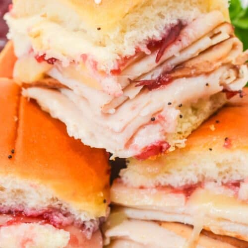 Three stacked Cranberry Turkey Sliders feature melted cheese and cranberry sauce nestled on soft dinner rolls.