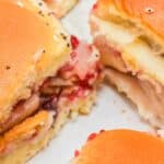 Close-up of Cranberry Turkey Sliders with golden buns, layers of turkey, bacon, cheese, and a vibrant red cranberry spread.