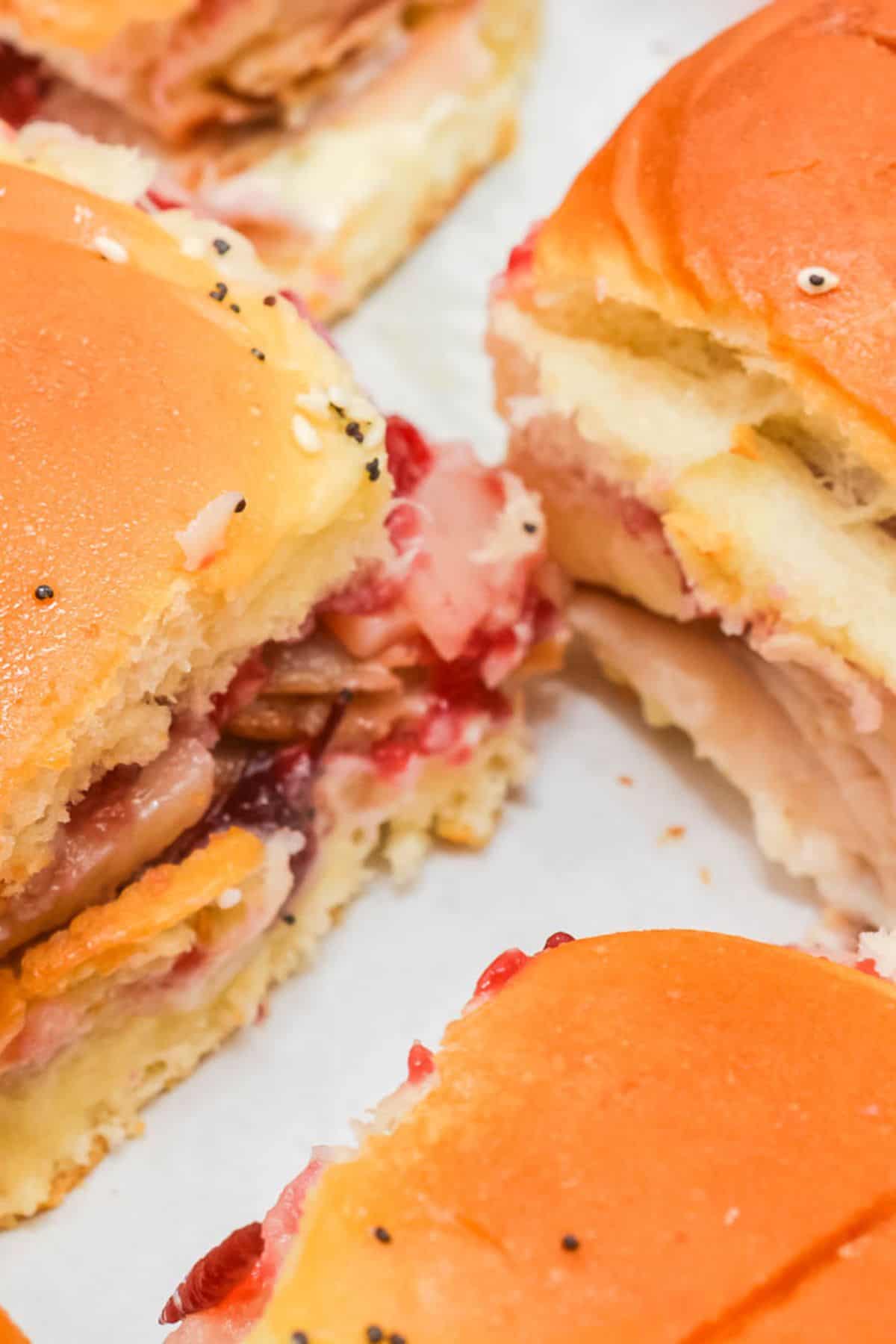 Close-up of Cranberry Turkey Sliders with golden buns, layers of turkey, bacon, cheese, and a vibrant red cranberry spread.