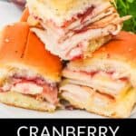Three Cranberry Turkey Sliders made with sliced turkey, cranberry sauce, and melted cheese on soft buns, stacked on a white plate with parsley garnish in the background.
