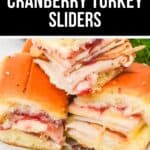 Three Cranberry Turkey Sliders on a white plate, made with layers of sliced turkey, cheese, and cranberry sauce on soft slider buns—perfect for your next gathering.