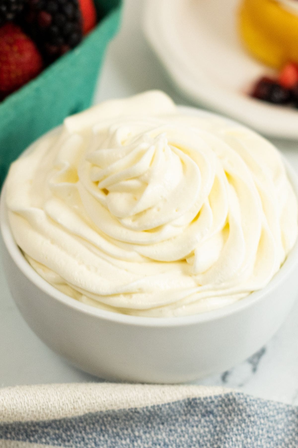 A white bowl  sits on a table near a basket of berries.