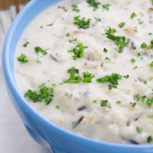 A blue bowl filled with creamy chicken and rice soup, garnished with chopped parsley.