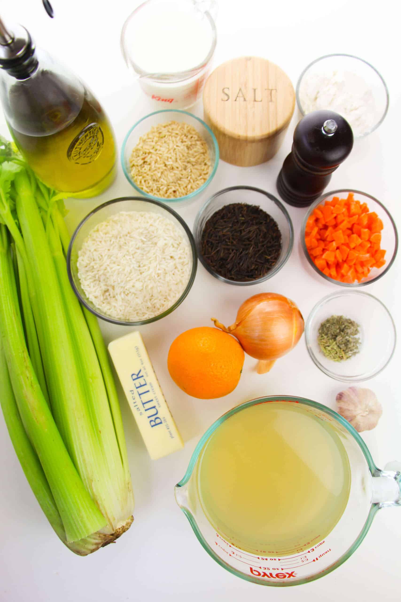Ingredients neatly arranged: celery, olive oil, salt, pepper, wild and white rice, diced carrots, flour, garlic, herbs, onion, orange. Butter and chicken broth add richness to the creamy chicken and rice soup accentuated by a splash of milk.