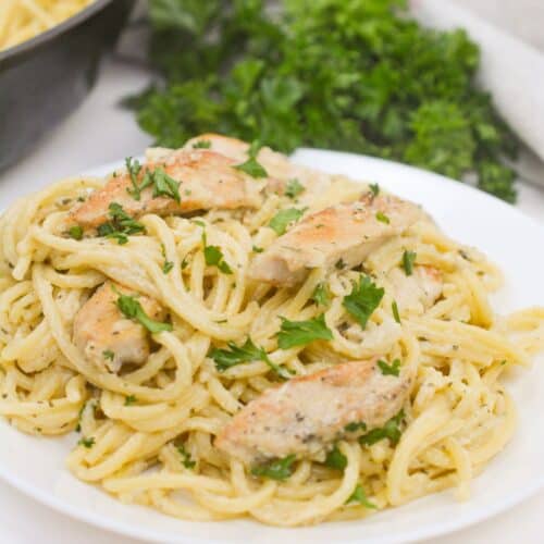 A plate of dinner garnished with chopped parsley, sits on a white plate with fresh parsley in the background.