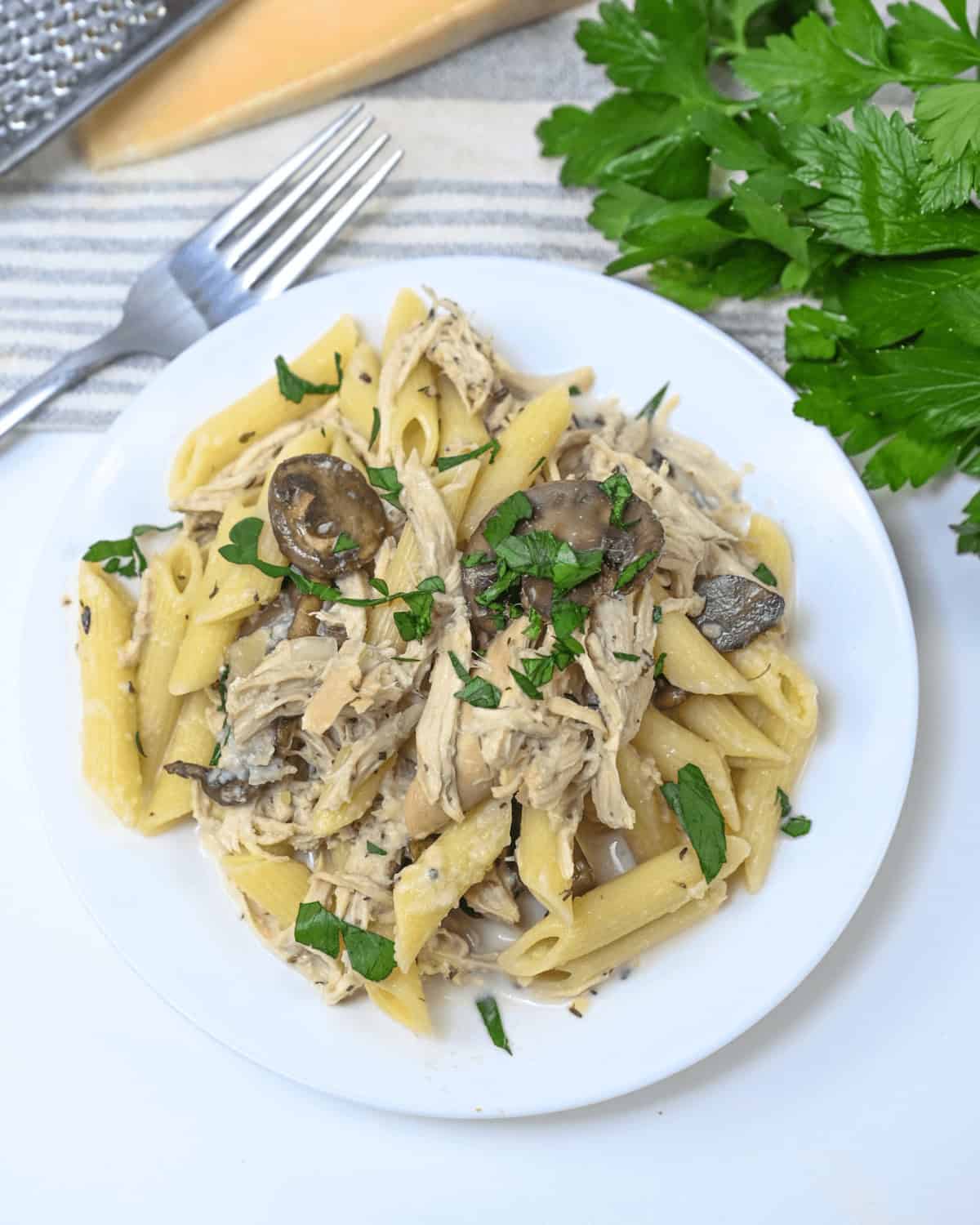Slow Cooker Chicken Pasta with mushrooms and parsley on a white plate.