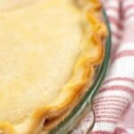 A close-up of a baked pie with a golden, crimped Crisco Pie Crust in a glass pie dish, resting on a red and white striped cloth.