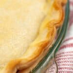 A close-up of a baked pie with a golden-brown, crimped Crisco Pie Crust in a glass dish, resting on a red and white striped cloth.