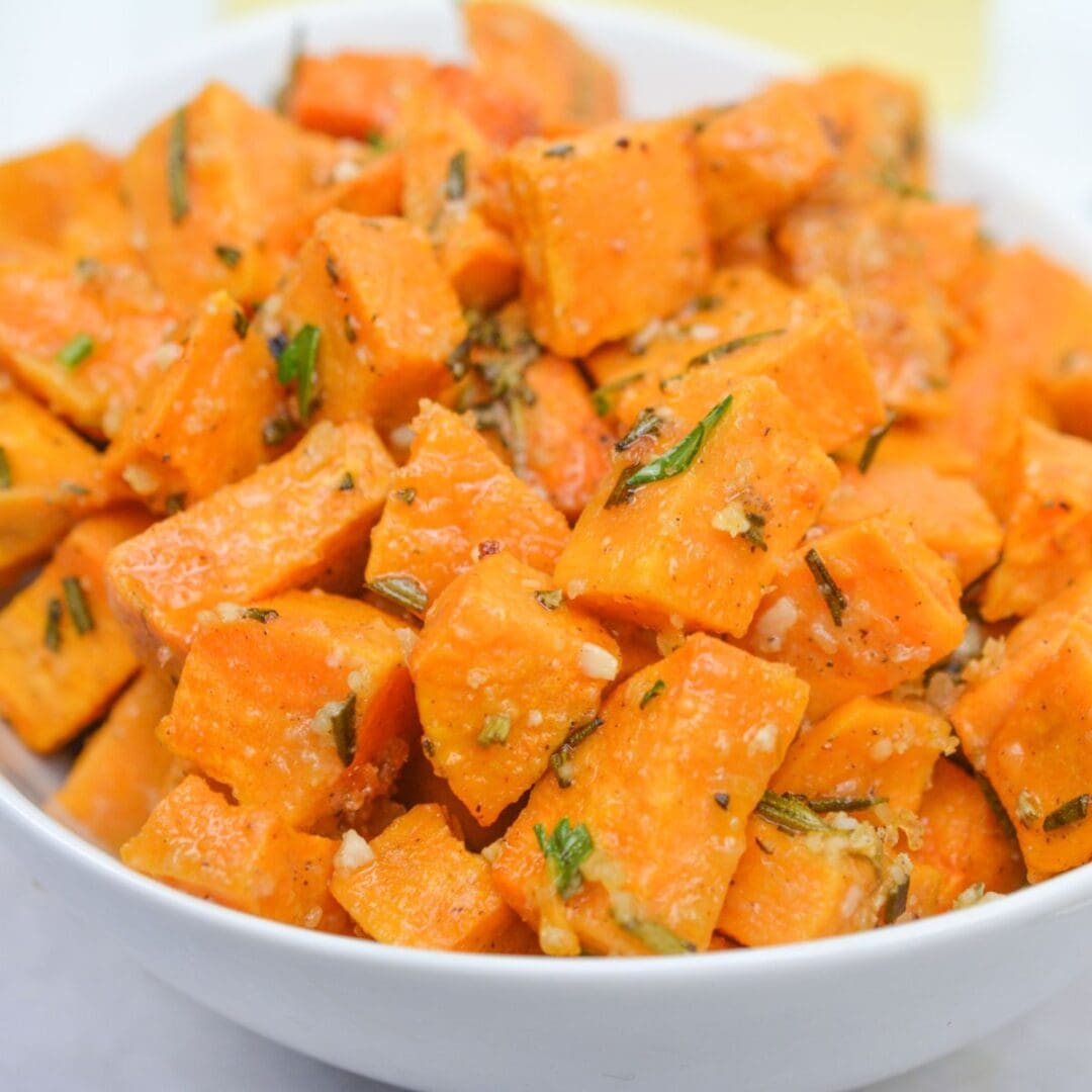 A white bowl filled with roasted sweet potato cubes, seasoned with herbs and spices—perfect for any savory sweet potatoes recipe.