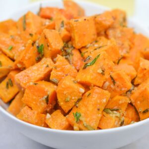 A white bowl filled with roasted sweet potato cubes, seasoned with herbs and spices—perfect for any savory sweet potatoes recipe.