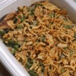 A casserole dish filled with Crock Pot Green Bean Casserole, topped with crispy fried onions and served with a wooden spoon on the side.