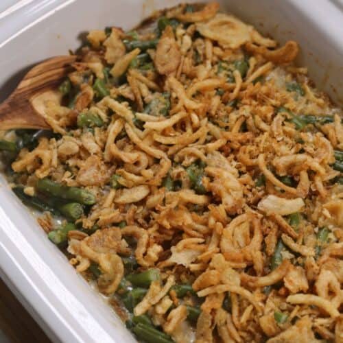 A casserole dish filled with Crock Pot Green Bean Casserole, topped with crispy fried onions and served with a wooden spoon on the side.