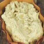 A serving dish filled with creamy Crock Pot Mashed Potatoes, topped with a sprinkle of black pepper.