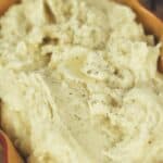 A serving dish filled with creamy Crock Pot Mashed Potatoes, topped with a sprinkle of black pepper.