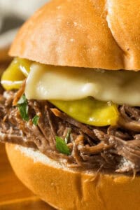 Enjoy a delightful Mississippi Pot Roast sandwich featuring shredded beef, melted cheese, and pickles nestled in a bun.