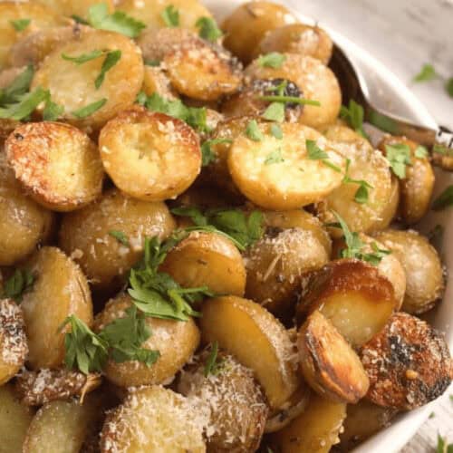 A bowl of sliced, roasted Crock Pot red potatoes garnished with grated cheese and fresh parsley.
