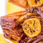 Stacked crock pot spiral honey-glazed ham slices garnished with caramelized orange slices.