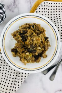A plate of Crock Pot Stuffing with pieces of mushrooms sits on a white plate with a dotted border, surrounded by patterned napkins and two forks.