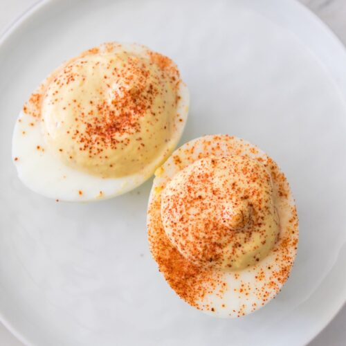 Two deviled eggs without mayonnaise, topped with paprika, are served on a white plate.