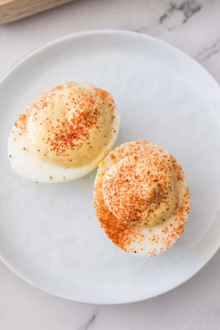 Two deviled eggs without mayonnaise, topped with paprika, are served on a white plate.