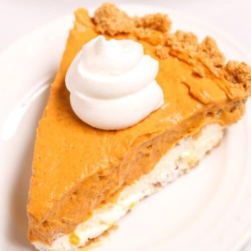 A slice of cream cheese pumpkin pie with a dollop of whipped cream on top, served on a white plate.