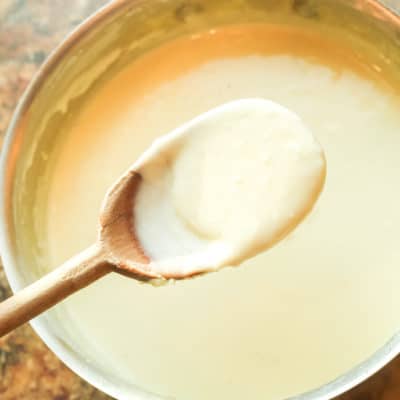 Traditional alfredo sauce on a spoon over a pot.