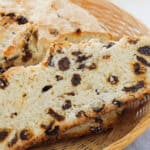 A slice of raisin bread, reminiscent of easy Irish soda bread, rests in a wicker basket with a butter package visible in the background.