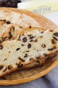 A slice of raisin bread, reminiscent of easy Irish soda bread, rests in a wicker basket with a butter package visible in the background.