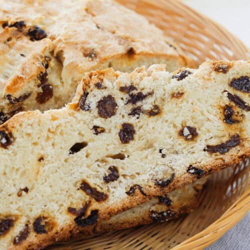 A slice of raisin bread, reminiscent of easy Irish soda bread, rests in a wicker basket with a butter package visible in the background.