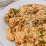 A plate of cheesy casserole, reminiscent garnished with chopped herbs and grated parmesan cheese.