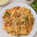 A plate of sausage risotto topped with grated cheese and chopped herbs, with a bowl of extra cheese and a pepper grinder nearby.