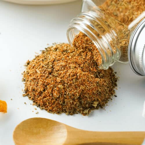 A jar of French fry seasoning on a table with a wooden spoon.