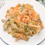 A serving of French’s Green Bean Casserole topped with crispy fried onions sits on a white plate.