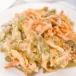 A serving of French’s Green Bean Casserole topped with crispy fried onions sits on a white plate.
