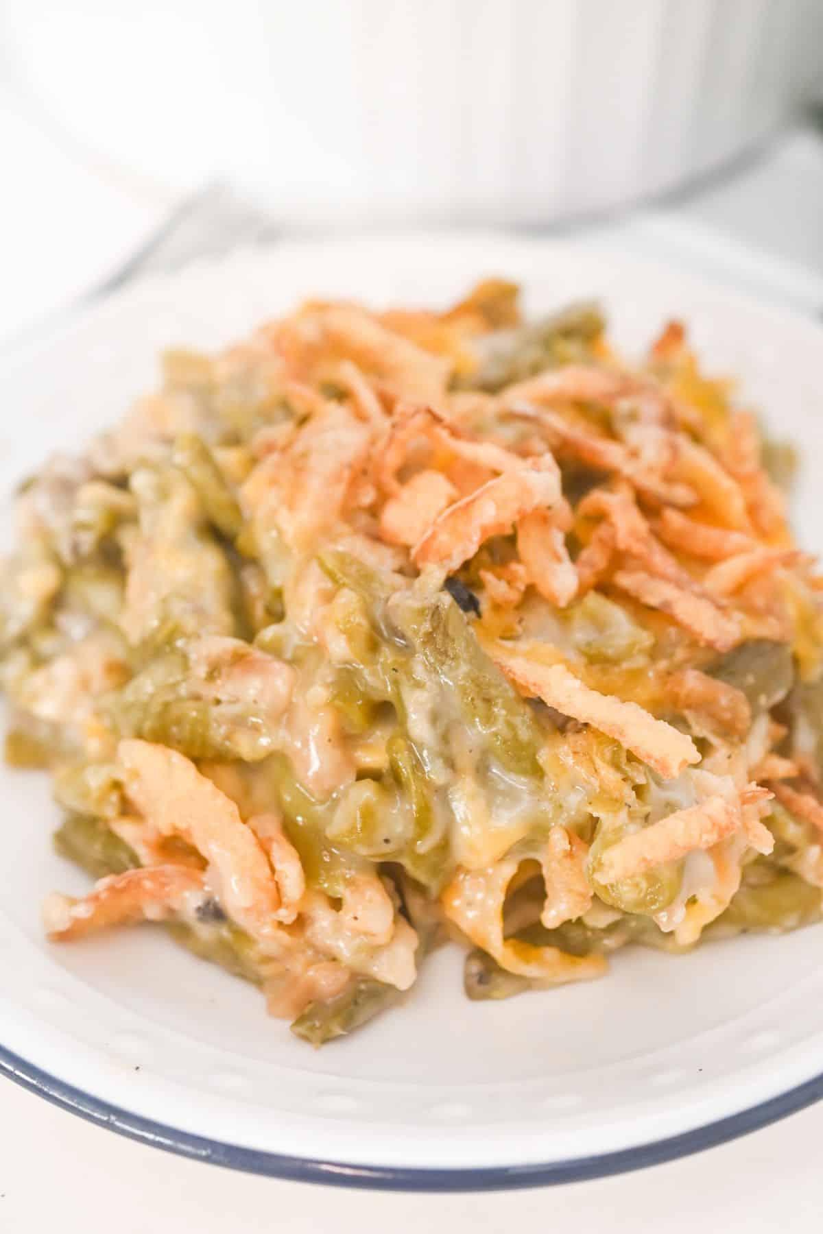 A serving of French’s Green Bean Casserole topped with crispy fried onions sits on a white plate.