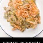 A serving of French’s Green Bean Casserole topped with crispy fried onions sits on a white plate, accompanied by a fork and fresh parsley. Text at the bottom reads "French’s Green Bean Casserole.