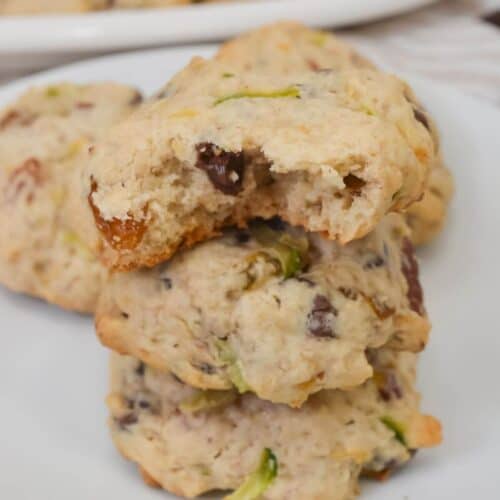 A stack of three with visible chocolate chips and green pieces, one with a bite taken out, sits on a white plate with more in the background.