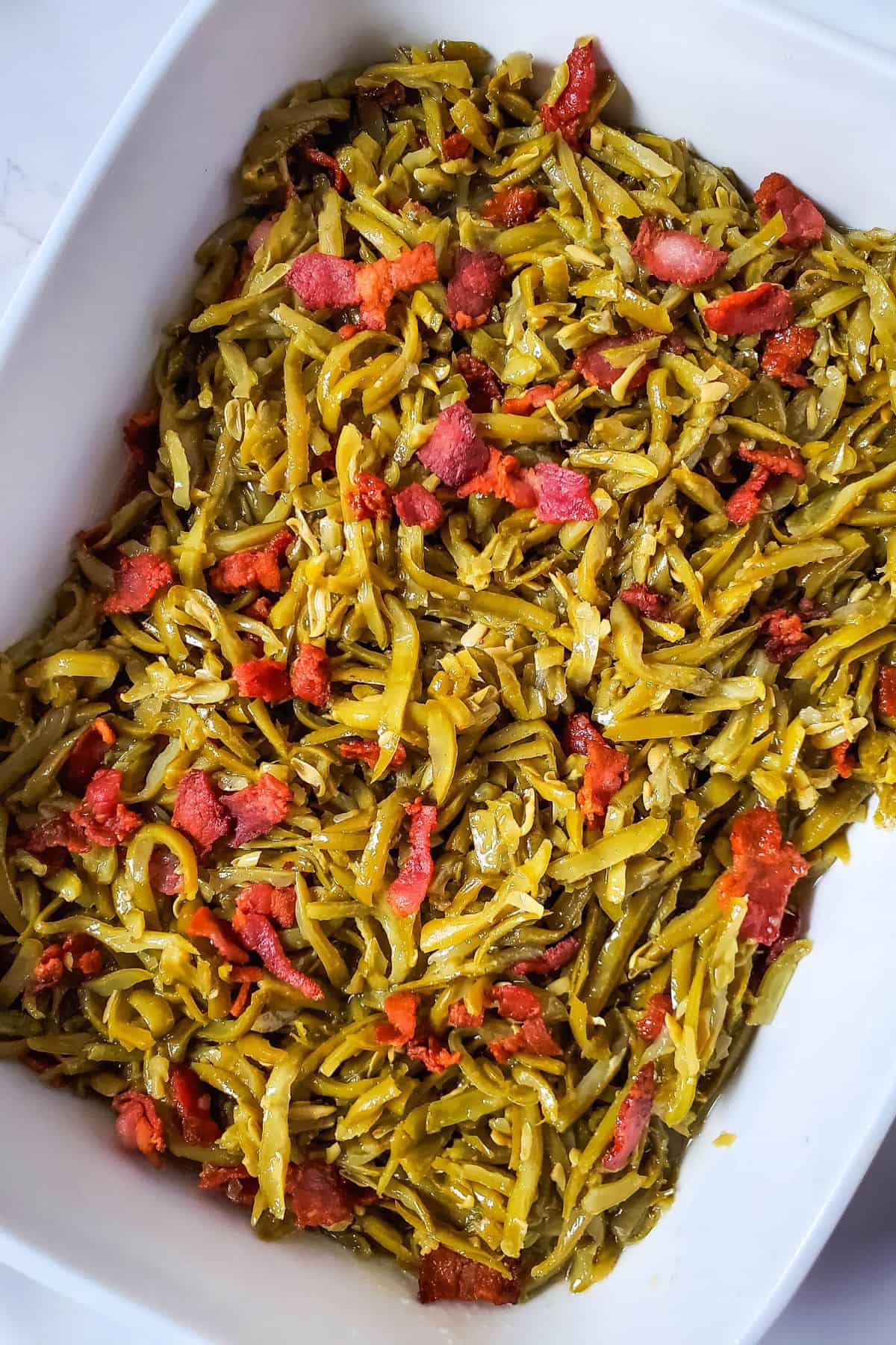 A white dish filled with Green Beans with Bacon and Onion, featuring tender green beans mixed with savory bacon pieces and caramelized onions.
