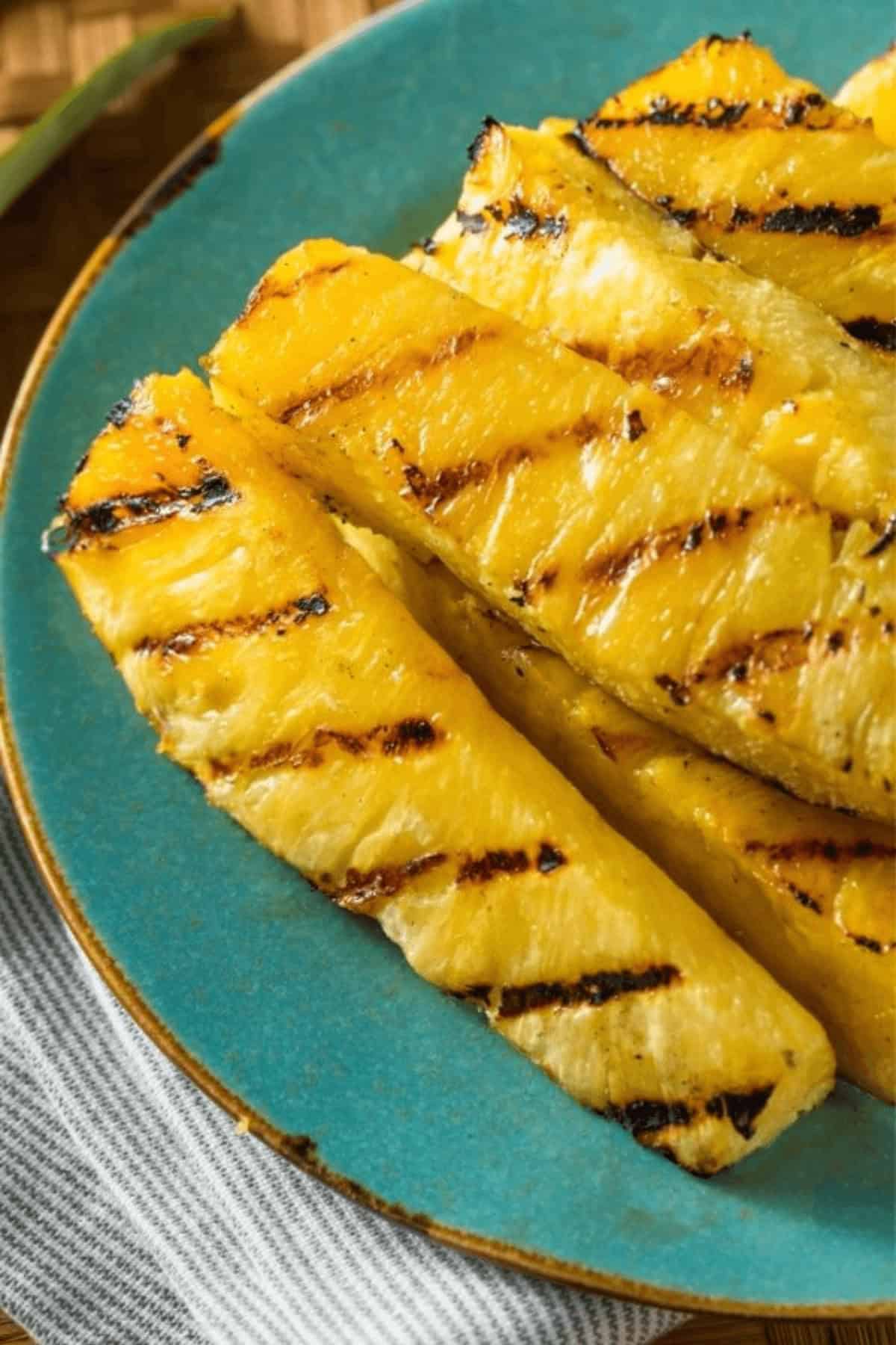 Grilled pineapple slices on a blue plate, displaying perfect grill marks and a golden-brown char.