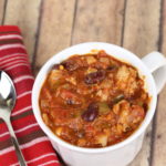 A cup of Ground Turkey Chili in a white mug with a spoon and a stripped napkin.