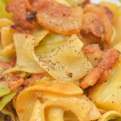 Close-up of a plate of Haluski (Cabbage and Noodles) featuring egg noodles, tender cabbage, and pieces of browned sausage, all seasoned with freshly ground black pepper.