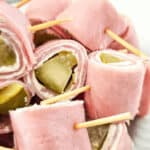 Pickle Roll Ups feature ham rolled with creamy cheese and tangy pickles, all neatly secured with toothpicks on a pristine white plate.