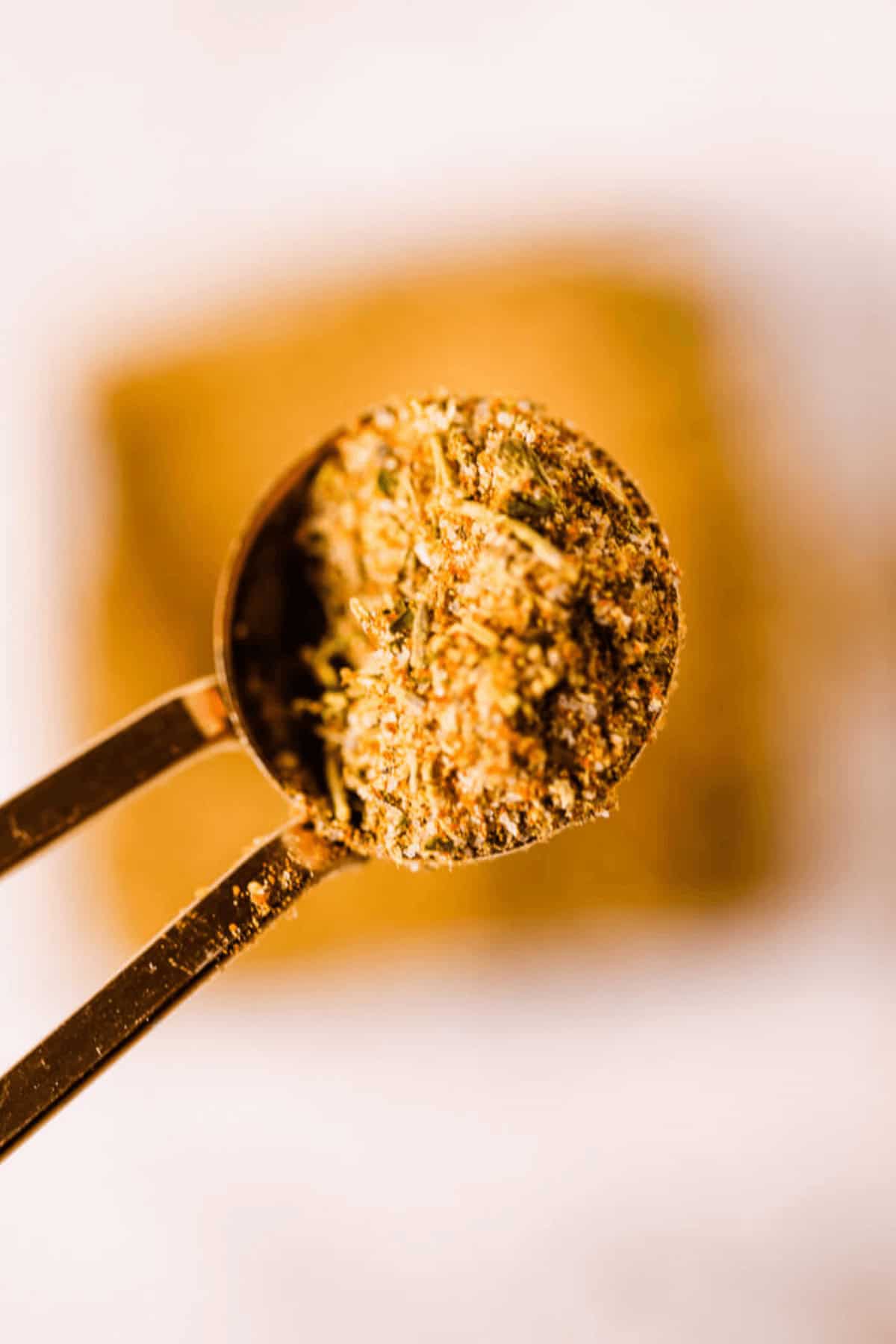 Close-up of a teaspoon filled with vibrant yellow homemade chili seasoning, with a beautifully blurred background.