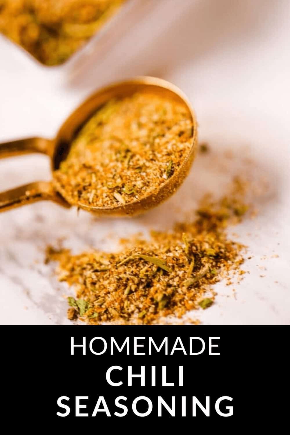 A gold measuring spoon overflows with homemade chili seasoning, its vibrant blend cascading onto the cool marble surface. Subtle hints of spice beckon the adventurous palate. A text reads: "Homemade Chili Seasoning.