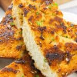 Two slices with a crispy, golden-brown top and sprinkled with chopped herbs, served on a white plate.